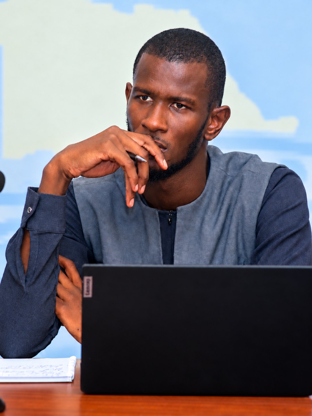 Aziz Diao seated at a table, a pen raised to his chin, a laptop in front of him